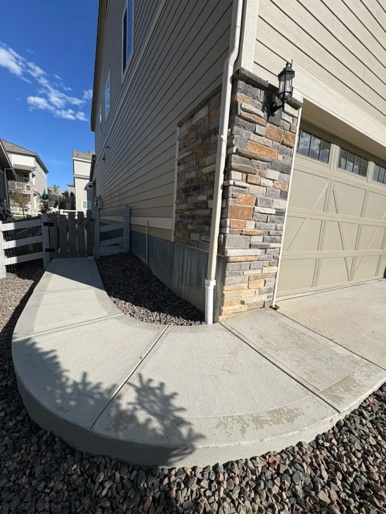 Curved concrete sidewalk wrapping a garage corner with rock landscaping
